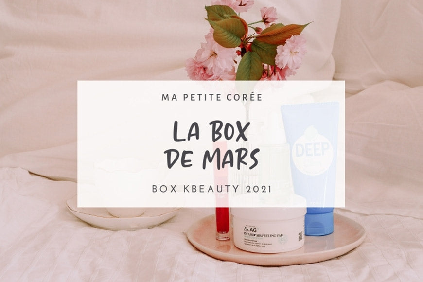 Produits de LA KBEAUTY BOX DE MARS 2021 avec crèmes et fleurs sur un plateau blanc.