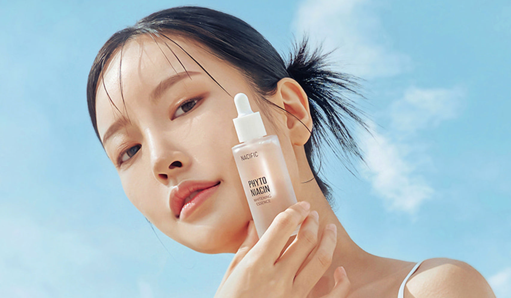 Femme tenant un sérum NACIFIC, La Beauté Marine à Votre Portée, avec ciel bleu en arrière-plan.