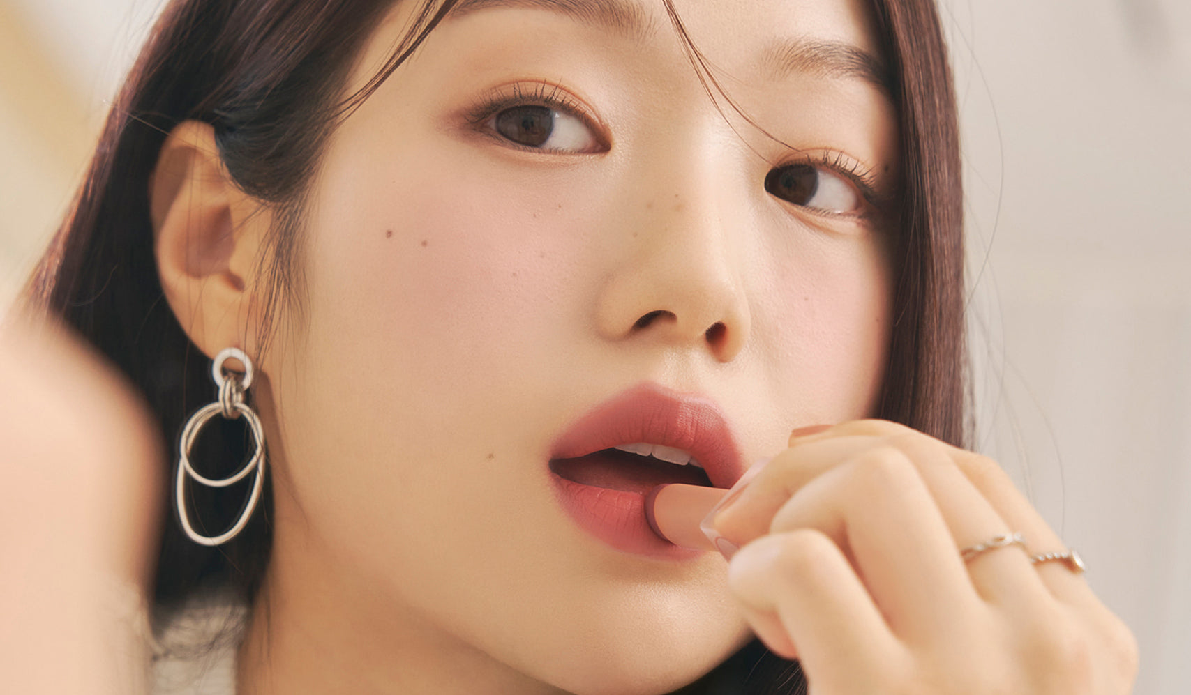 L'Univers Charmant de ROMAND: Femme appliquant un rouge à lèvres ROMAND, incarnant l'élégance et le charme naturel coréen.