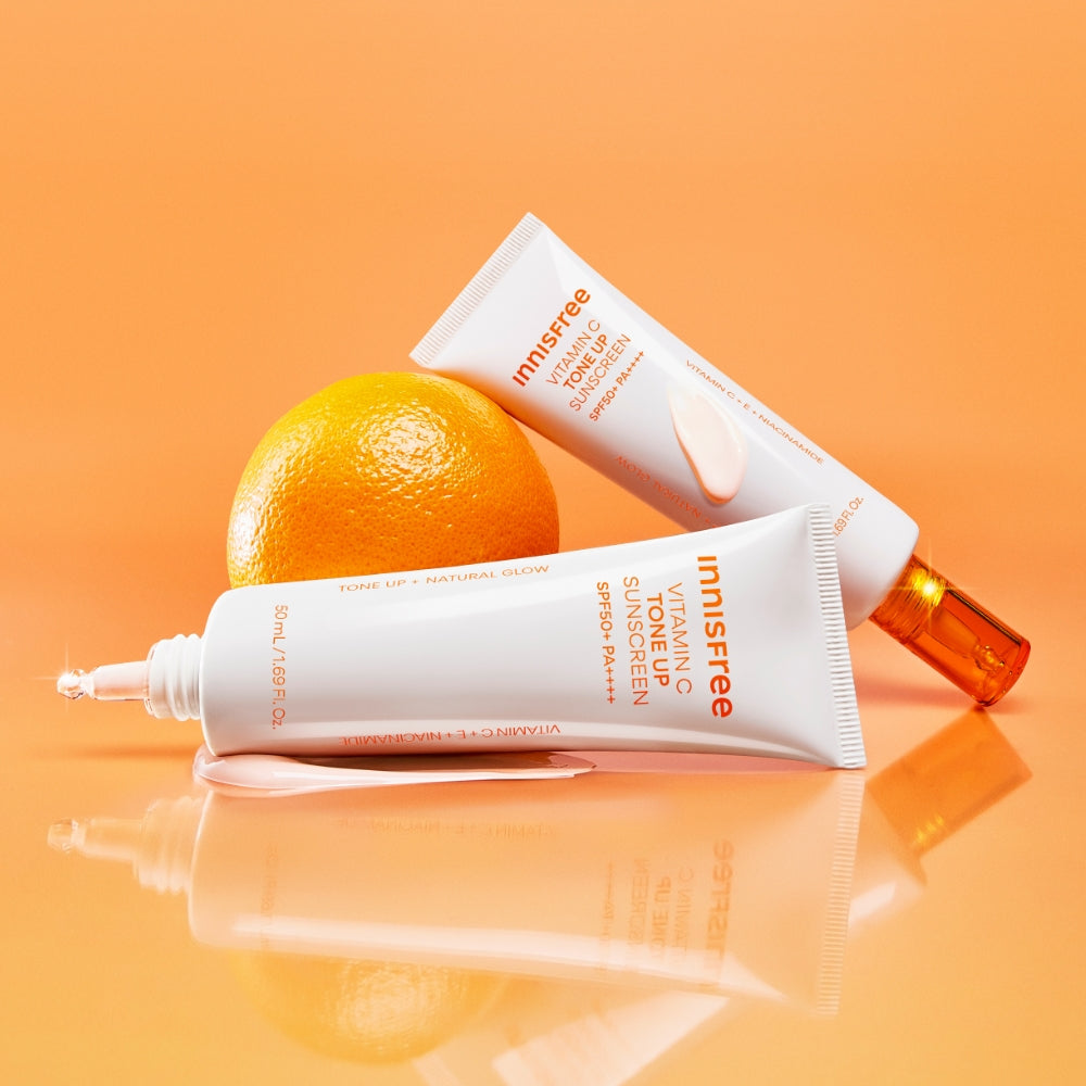 INNISFREE Vita C Spot Tone Up Sunscreen SPF50+/PA++++ 50ml, flacons et tube sur fond orange, agrumes et soleil