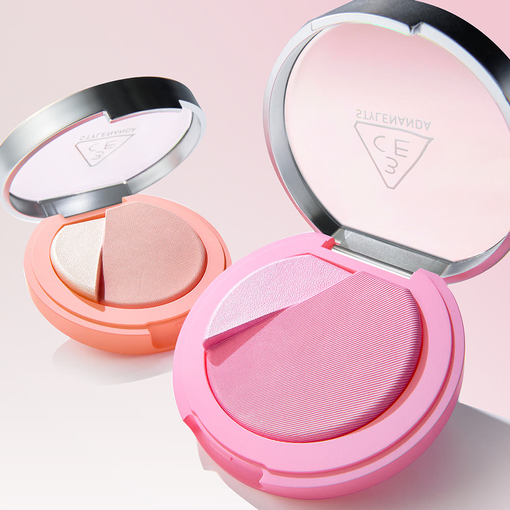 3CE Blushlighter de 3CE, blush et highlighter en palette ouverte, teintes roses, fond rose pastel, maquillage.