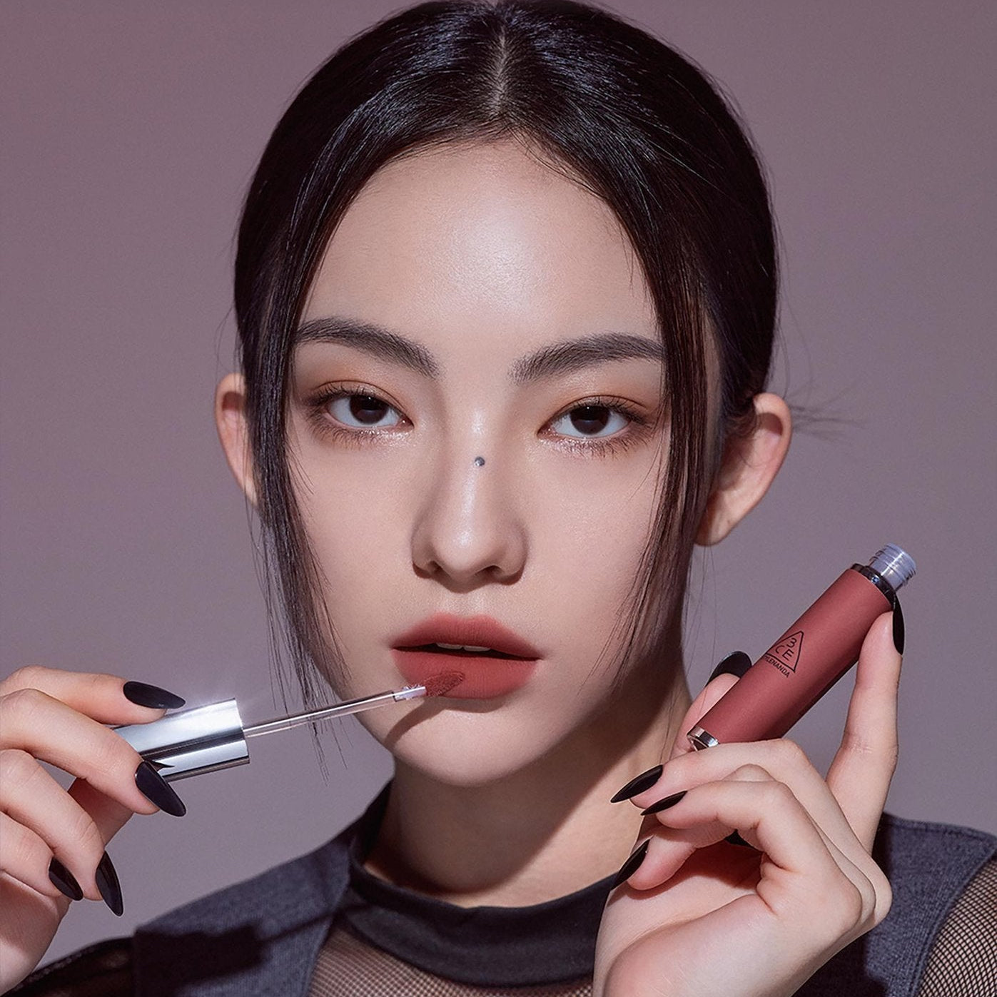 3CE Hazy Lip Clay, maquillage lèvres hazy: la marque 3CE tenant le produit sur fond violet, maquillage nude