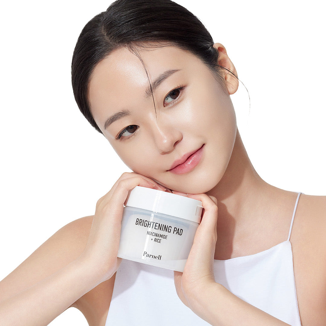 PARNELL Niacinamide Rice Brightening 60 pads, produit de soin sur peau lumineuse, jeune femme tenant le pot blanc sur fond clair.