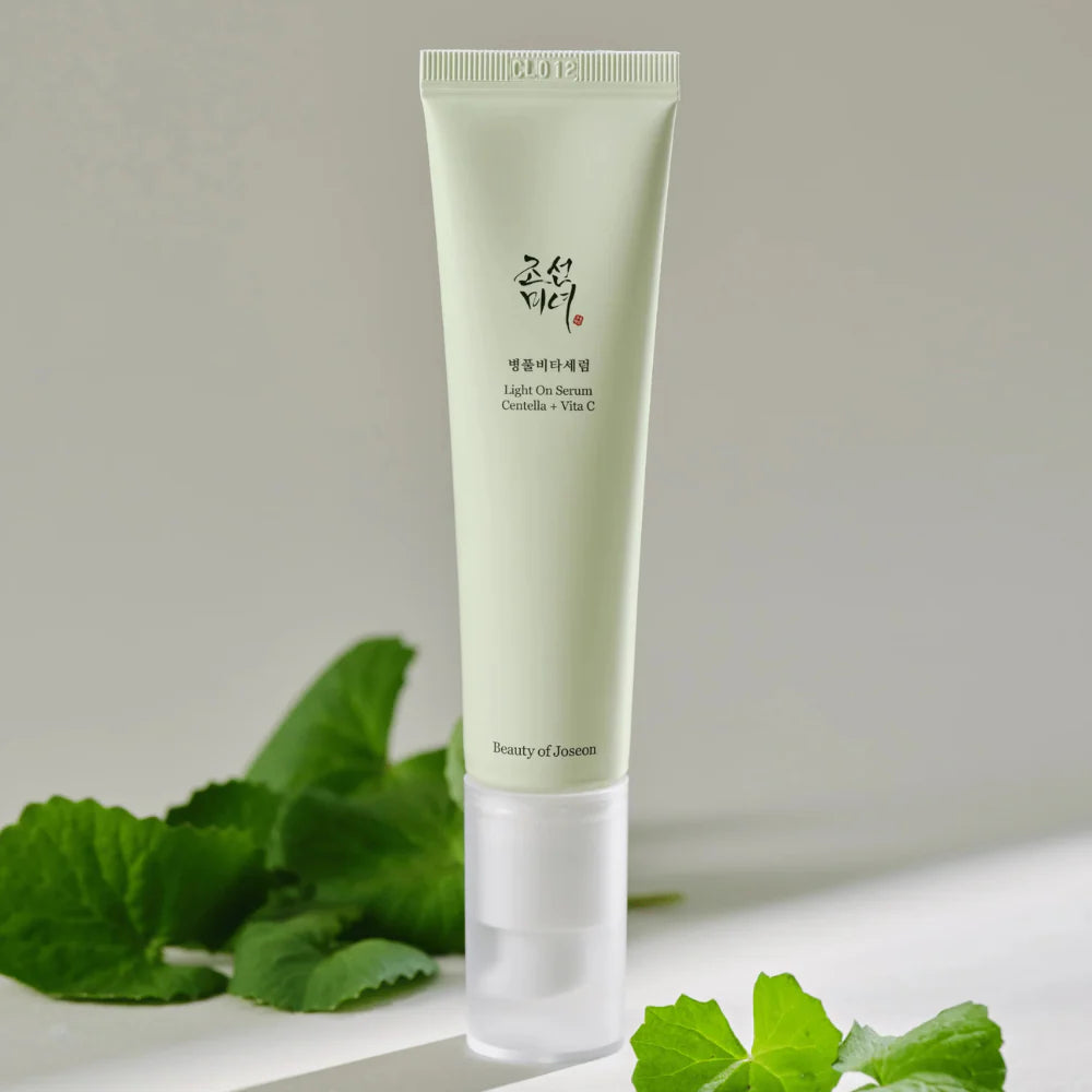 Décris l'image en français : BEAUTY OF JOSEON Light On Serum Centella+ Vita C 30ml sur fond beige avec feuilles vertes.