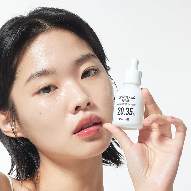 Décris l'image en français: PARNELL Niacinamide 20.35 Rice Brightening Serum 30ml, sérum lumineux, femme l’applique, flacon blanc.