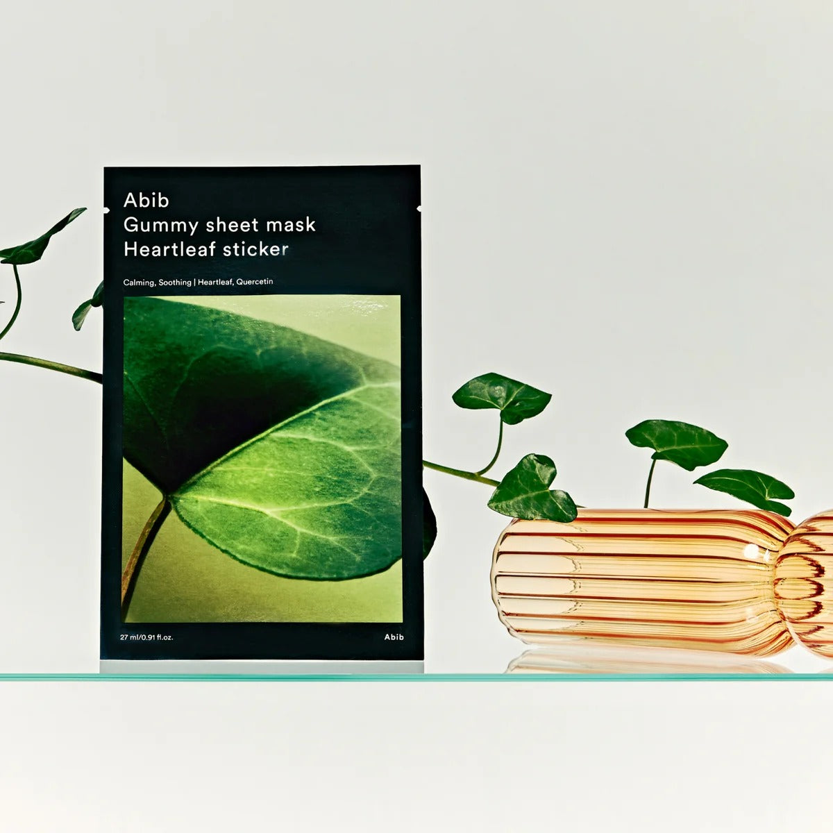 ABIB Gummy Sheet Mask Heartleaf Sticker 10 sheets sur une étagère en verre avec des feuilles vertes décoratives à côté.