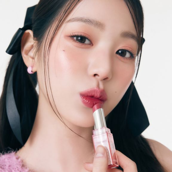 AMUSE Dew Balm : femme applique un baume rosé, gros plan maquillage, ambiance beauté sur fond clair