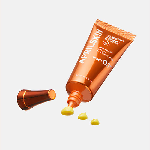 APRILSKIN Carrotene IPMP Clearing Solution d’APRILSKIN sur fond blanc, tube orange avec gouttes jaunes, produit skincare