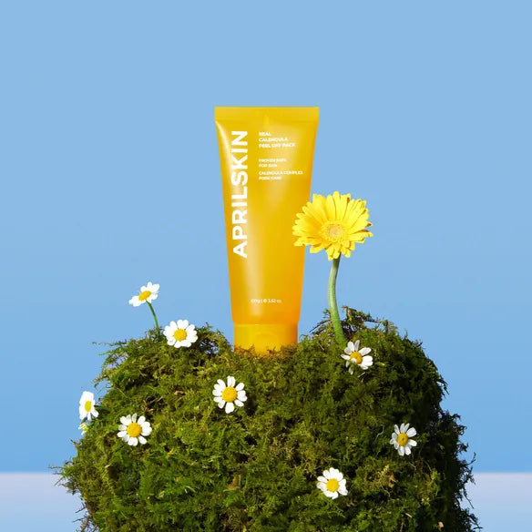 APRILSKIN Calendula Peel Off Pack 100g : tube de soin APRIL SKIN sur globe moussant, fleurs de souci jaunes et marguerites, fond bleu.