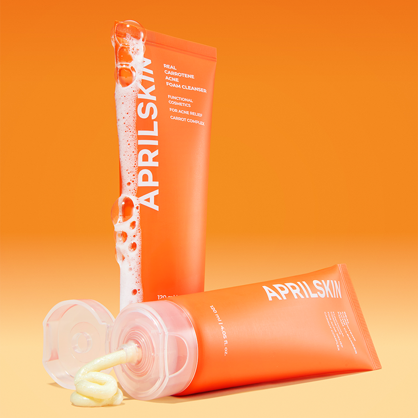 APRILSKIN Real Carrotene Acne Foam Cleanser 120ml d’APRILSKIN, flacon rose/orange, mousse sur fond orange lumineux.