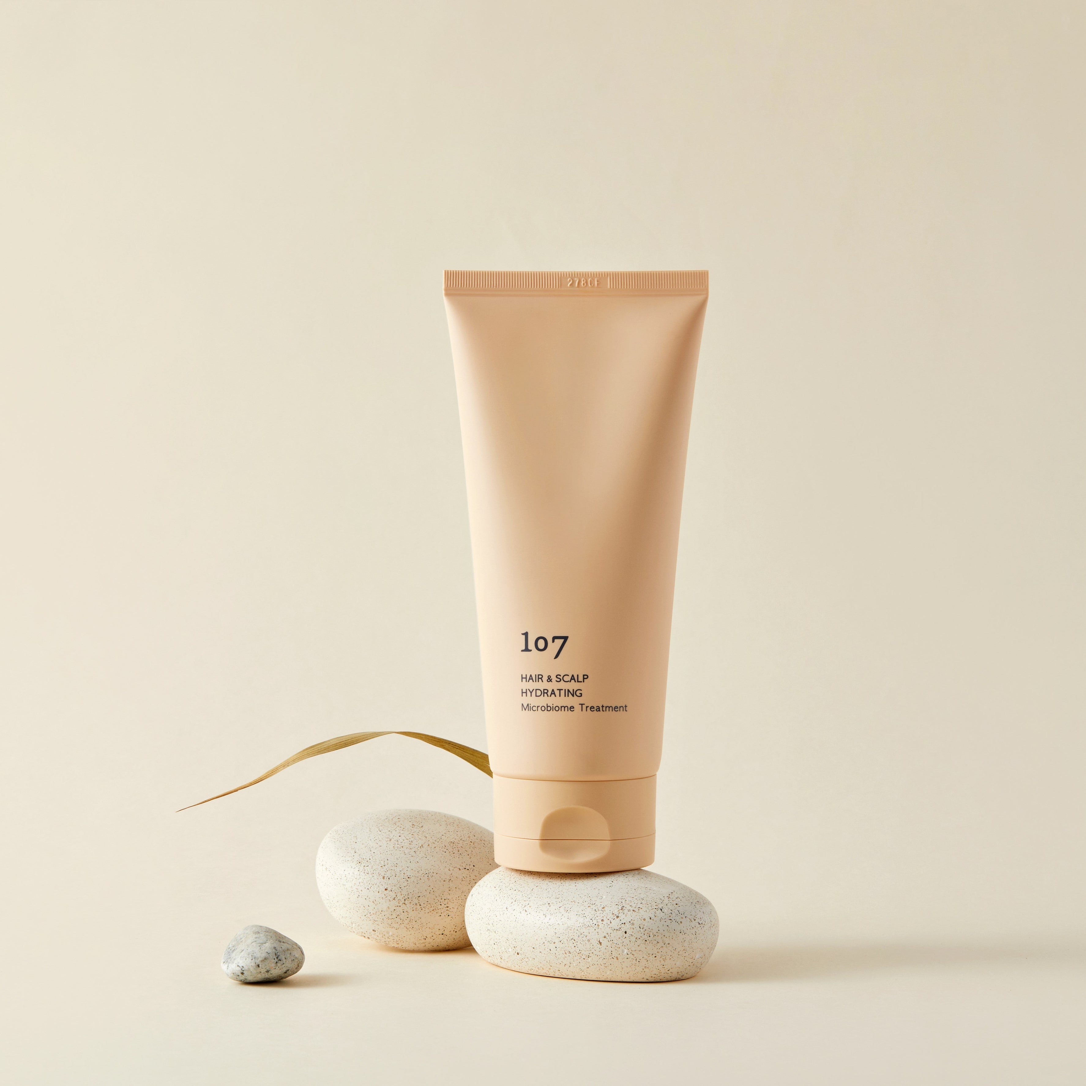 107 Hair & Scalp Hydrating Microbiome Treatment 180ml de la marque 107, tube crème sur pierres, fond beige.