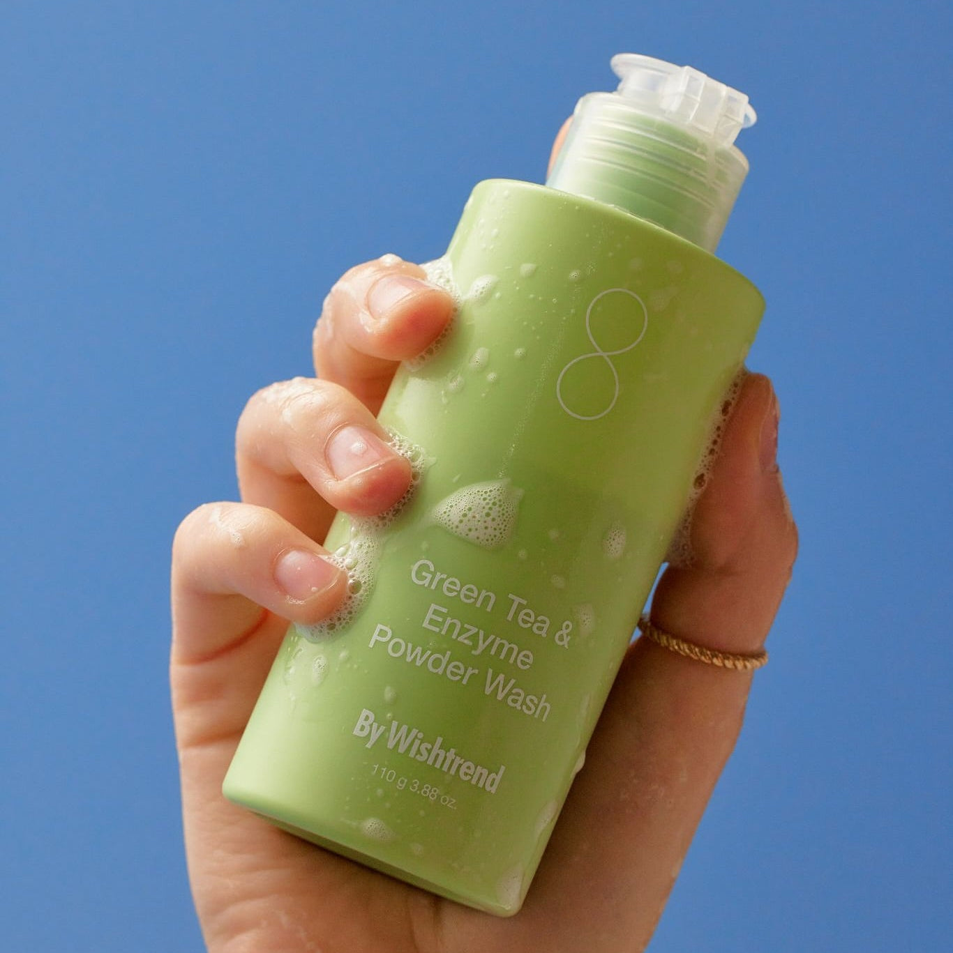 BY WISHTREND Green Tea & Enzyme Powder Wash 110g : flacon vert en main, fond bleu, vue produit.
