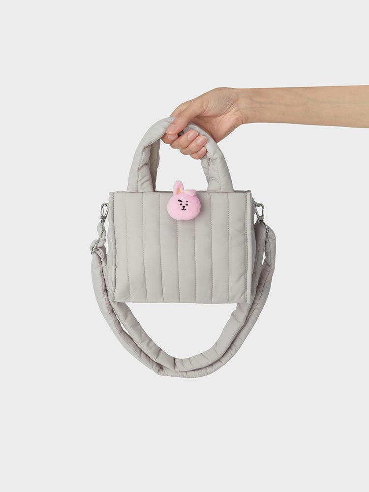 BT21 COOKY QUILTED BAG WITH FACE PLUSH BADGE WINTER EDITION, sac matelassé gris avec badge plush COOKY sur fond blanc.