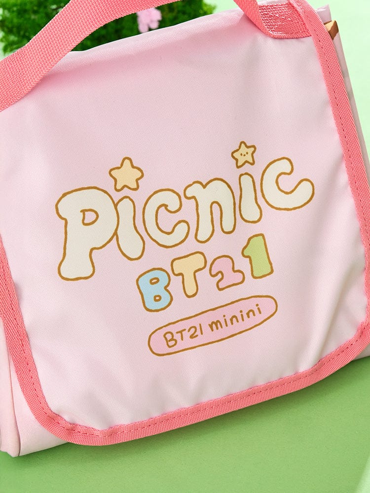 BT21 mini minini PICNIC MAT PICNIC MATE, sac de pique-nique officiel LINE FRIENDS, “Picnic BT21” rose, sur pelouse verte.