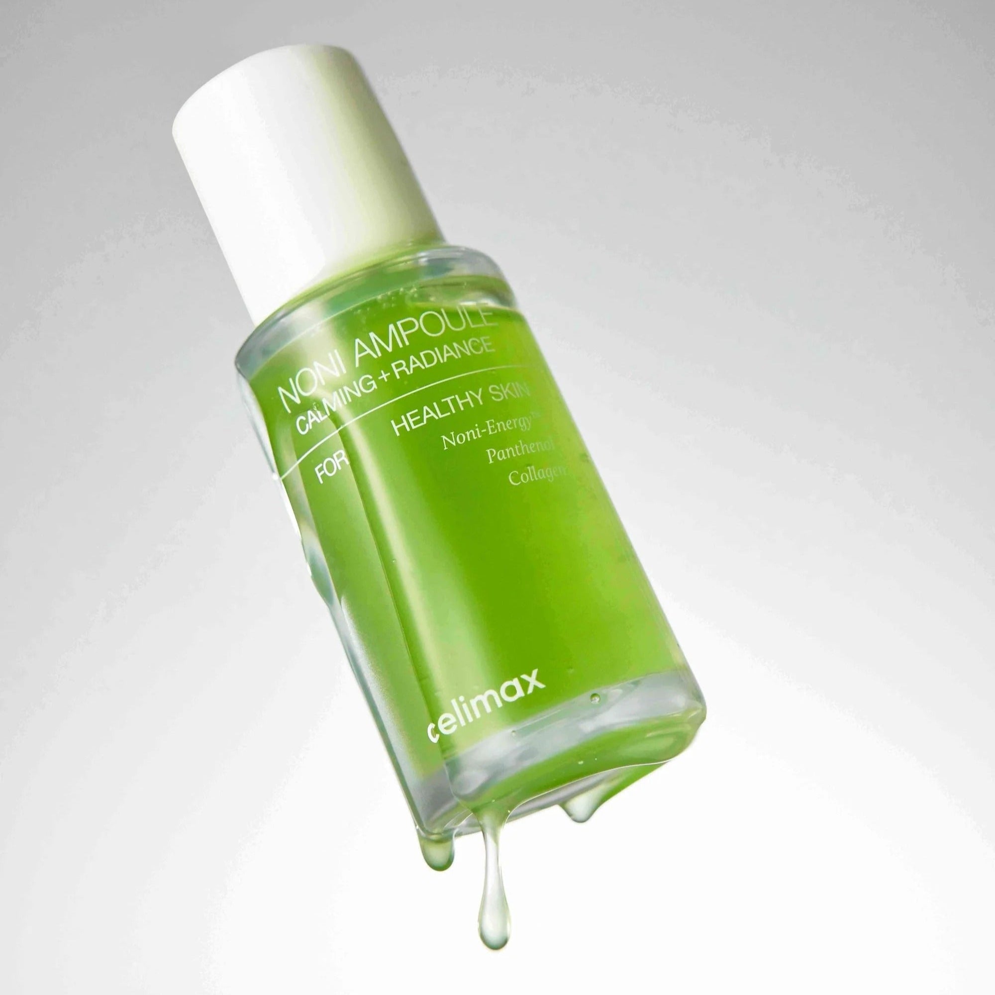 CELIMAX Noni Ampoule Calming+Radiance 100ml : flacon vert avec gouttes, produit beauté apaisant sur fond clair.