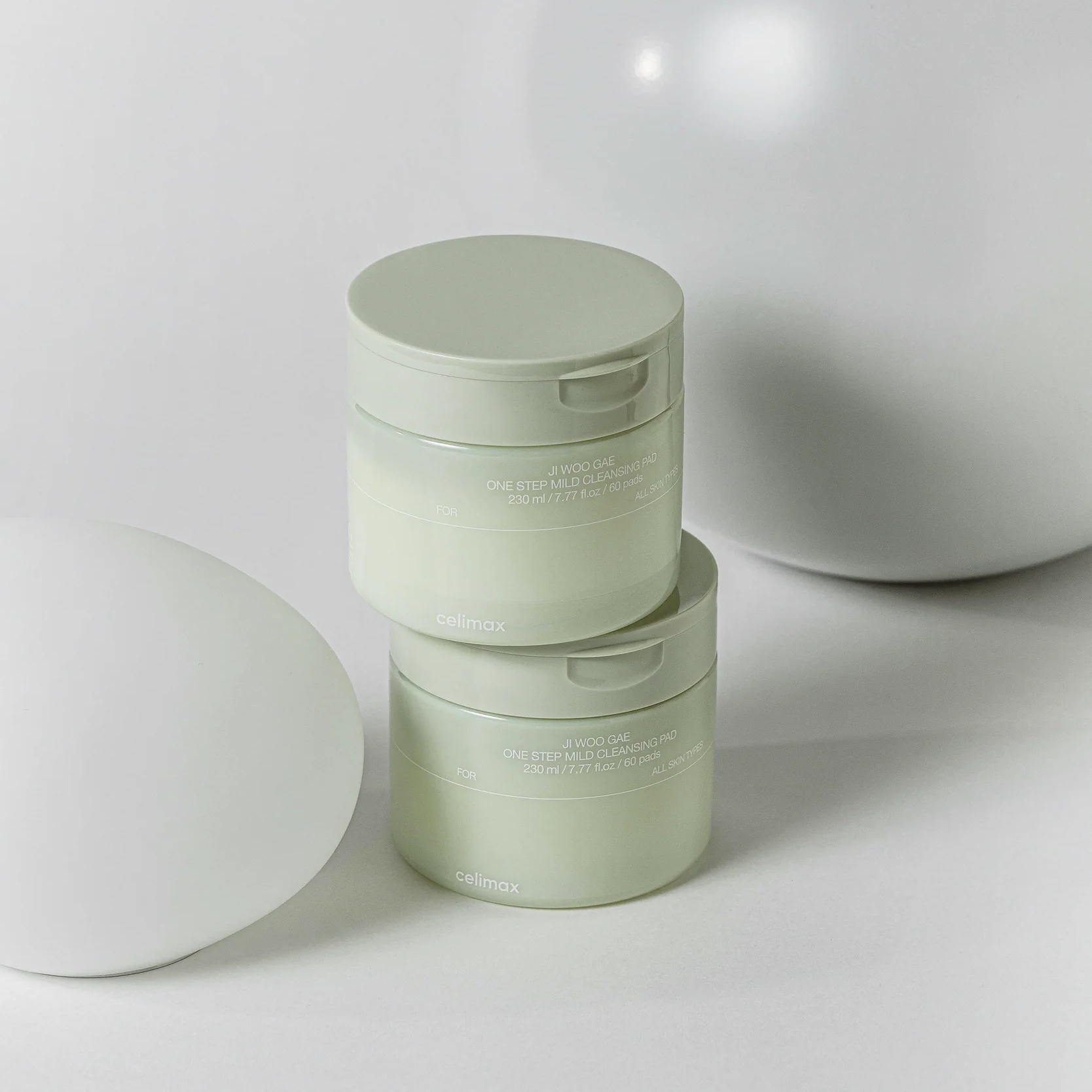 Deux pots de CELIMAX Ji Woo Gae One Step Mild Cleansing Pad 60 pads sur une surface beige élégante.