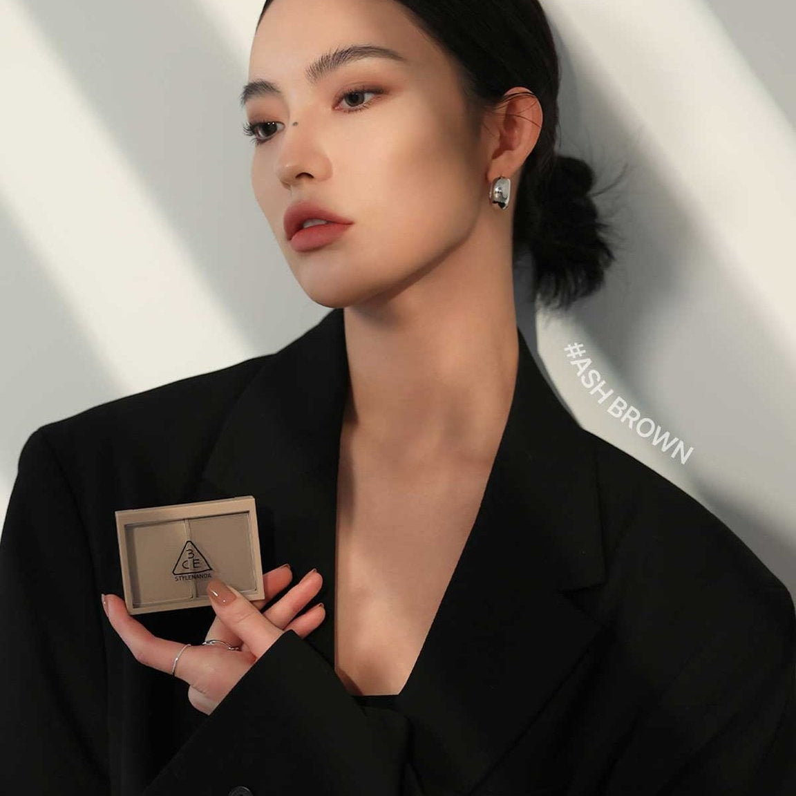Maquillage 3CE Contour Shading de 3CE, maquillage de contour sur une femme en tenue noire, fond clair.