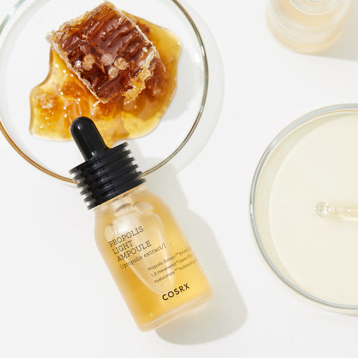 COSRX Full Fit Propolis Light Ampoule 30ml de COSRX, sérum à la propolis noire, sur fond blanc avec gouttes et flacon.
