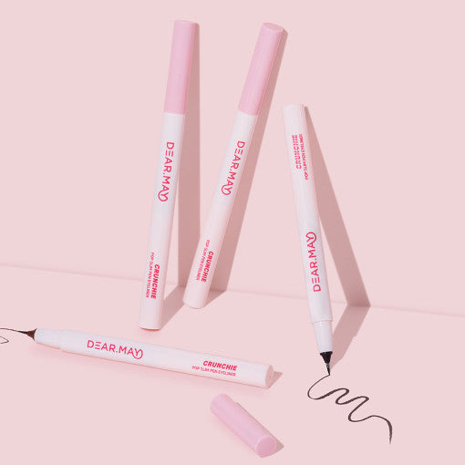 DEAR MAY Crunchie Pop Slim Pen Eyeliner DEAR MAY sur fond rose, stylos cosmétiques et trace d’eye-liner, maquillage.