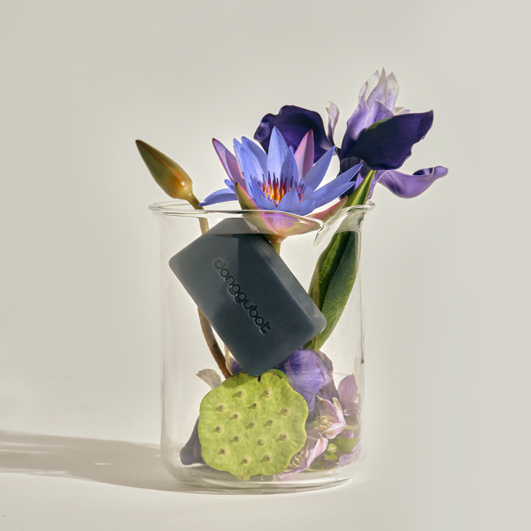 DONGGUBAT Field Blooming Perfume Shampoo Bar Repair 80g, savon shampooing en barre de marque, entouré de fleurs, fond clair.