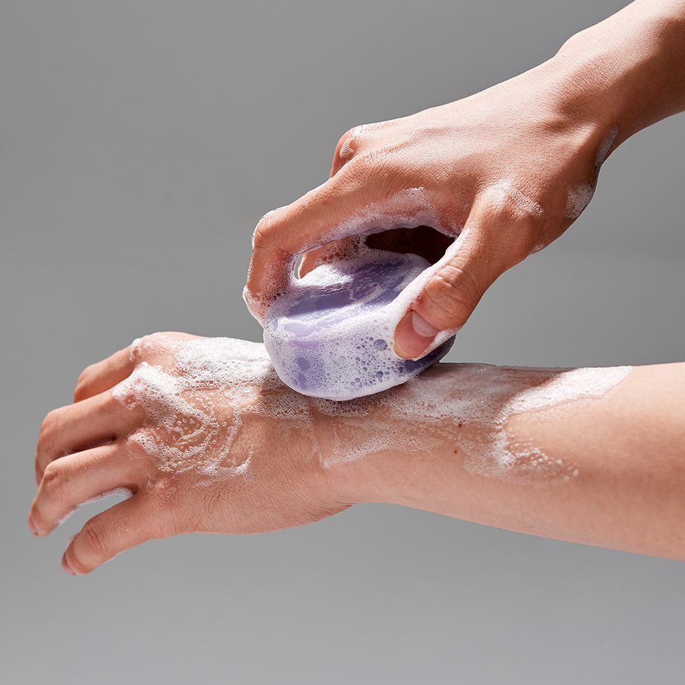 Décris l'image en français : DONGGUBAT Field Correct Cleansing Soap Collagen de la marque, mousse sur les mains sous douche.