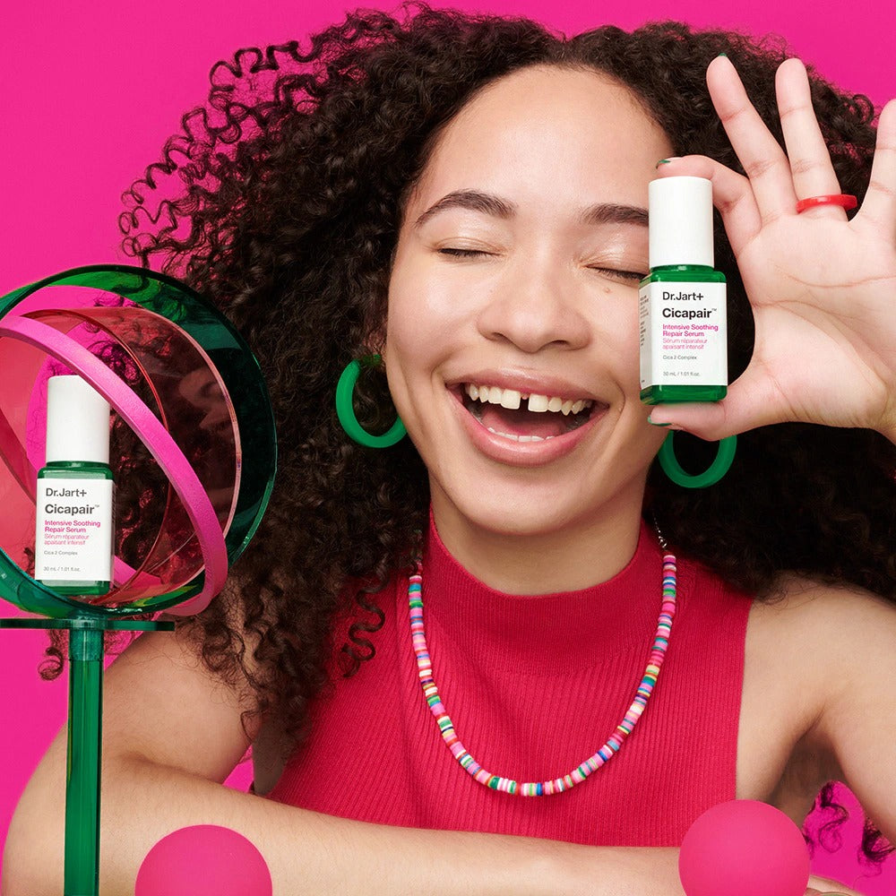 Sérum apaisant DR.JART+ CicapairI ntensive Soothing Repair Serum 30ml tenu par une femme souriante, fond rose vif.