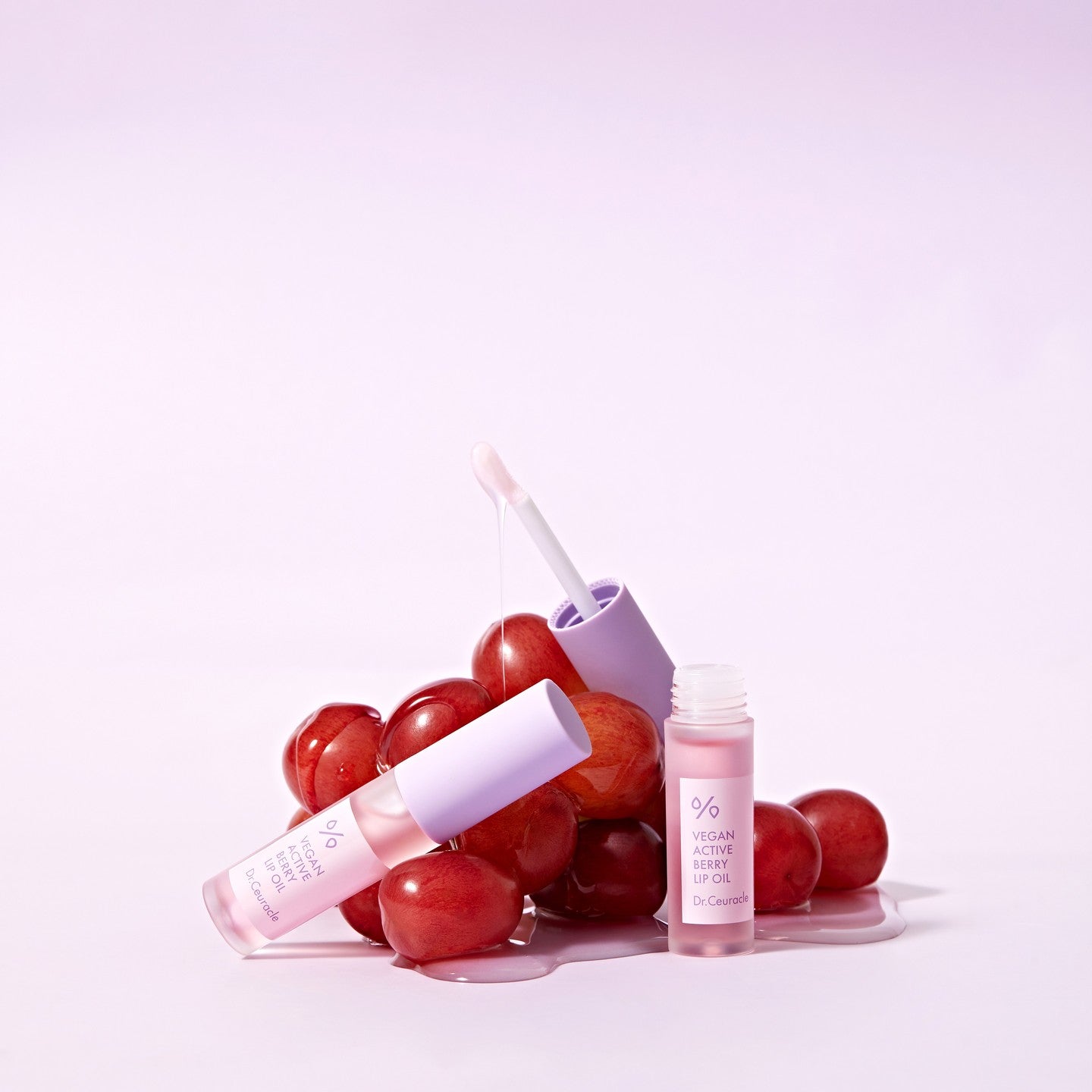 DR.CEURACLE Vegan Active Berry Lip Oil, flacon rose sur cerises rouges sur fond pastel, visuel produit en studio.
