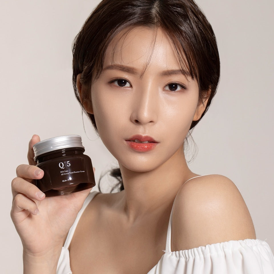 Femme tenant un pot de QUA-T Dia All Green Total Essence Cream 100ml, crème hydratante de qualité en main.