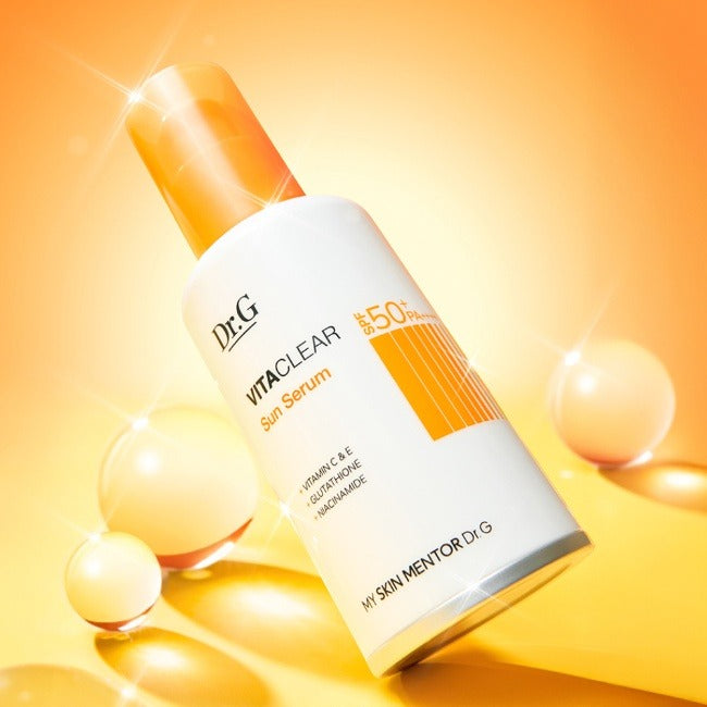 Décris l'image en français : Dr.G Vita Clear Sun Serum 50ml, flacon Dr.G sur fond lumineux orange, sphères dorées.