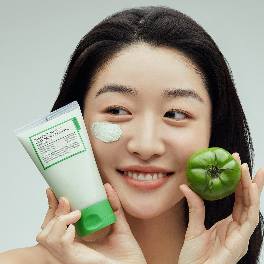 Femme souriante utilisant le FULLY Green Tomato Clay Pack Cleanser 120ml avec un visage frais et un tomate verte en main.