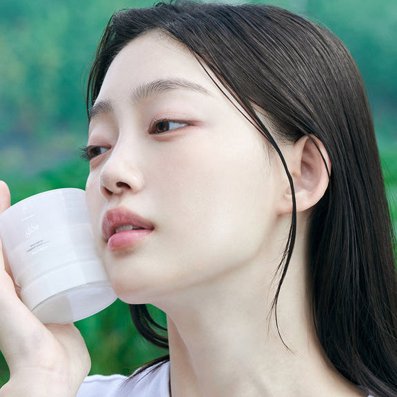 GLOW Aloe Barrier Support Cream 50ml de GLOW, pot blanc appliqué sur le visage d’une femme, ambiance spa extérieure.