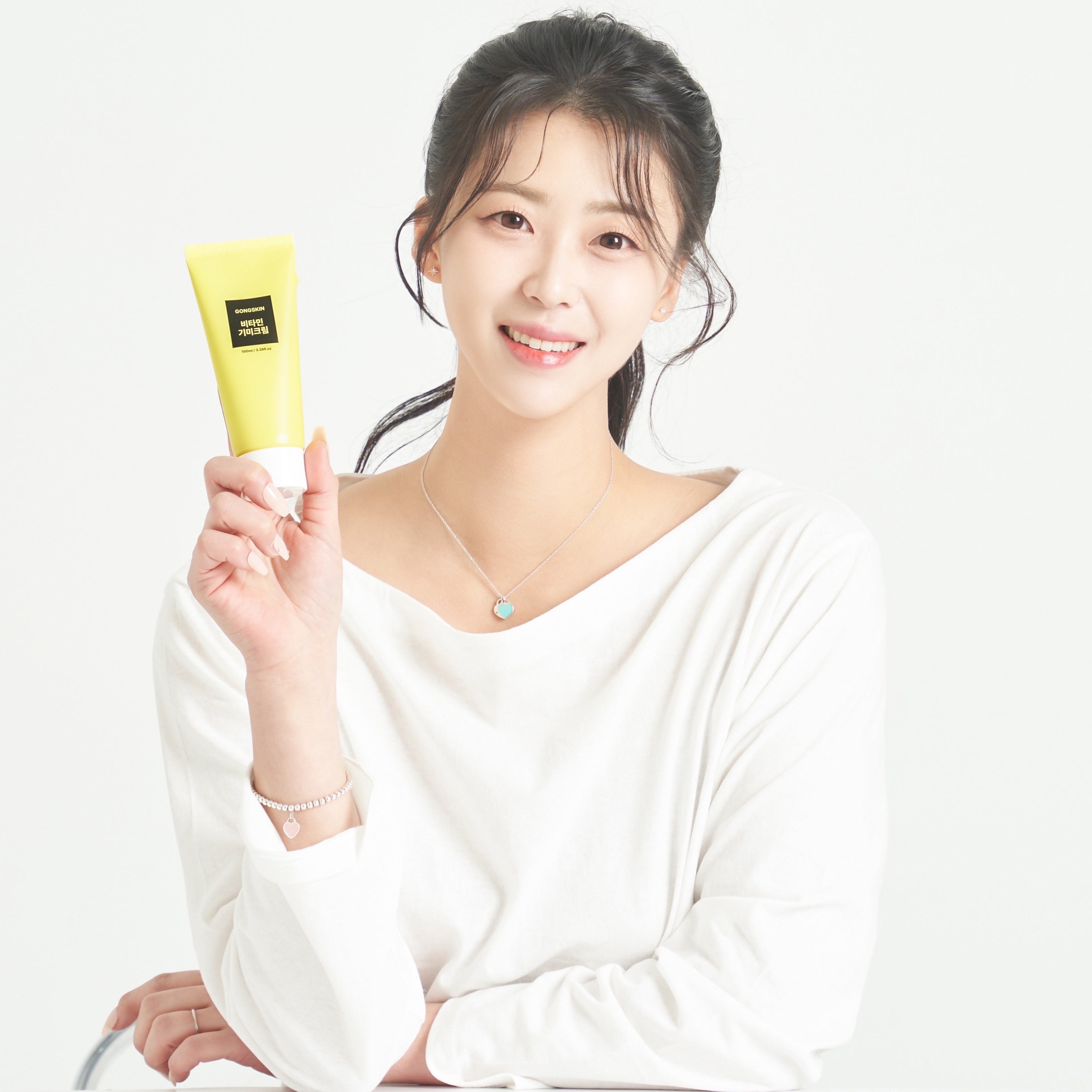 Femme souriante tenant un tube de crème GONGSKIN Vitamin Freckle Cream 100ml pour soin de la peau, posant en blouse blanche.