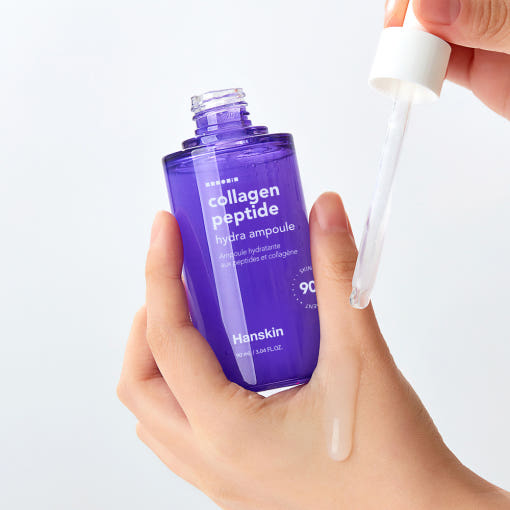 Décris l'image en français mentionnant HANSKIN Collagen Peptide Hydra Ampoule 90ml: flacon violet tenu dans les mains sur fond blanc.