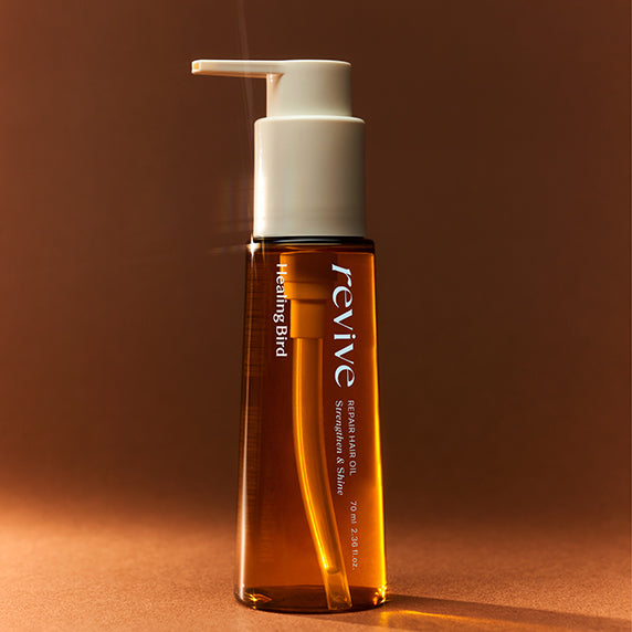 HEALING BIRD Revive Repair Hair Oil 70ml, flacon orange sur fond brun, marque et produit en gros plan.
