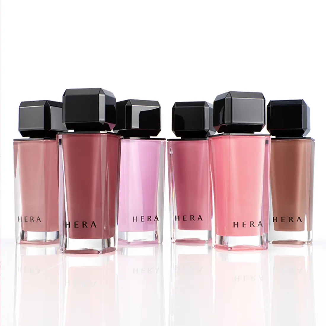 HERA Sensual Nude Gloss 5g : flacons HERA roses et nude sur fond clair, rendu maquillage brillant en studio.