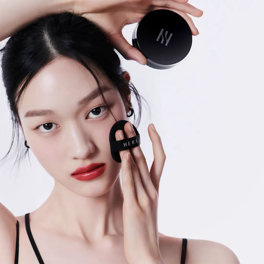 HERA Black Cushion Foundation SPF34 PA++ 15g de HERA, maquillage sur le visage d’une femme, coussin noir sur fond clair.