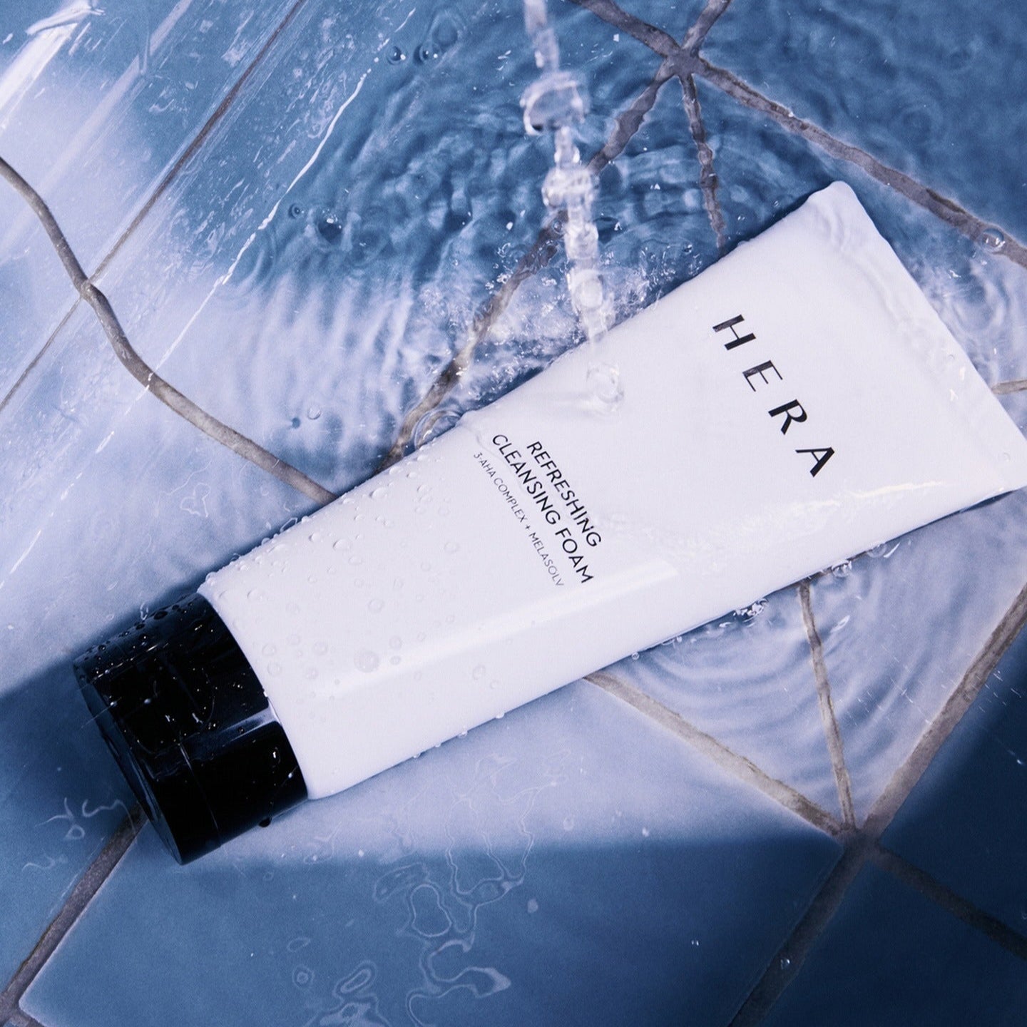 HERA Refreshing Cleansing Foam 160g sur fond de carrelage bleu mouillé, produit de soin visage, nettoyage revitalisant, beauté éclatante.