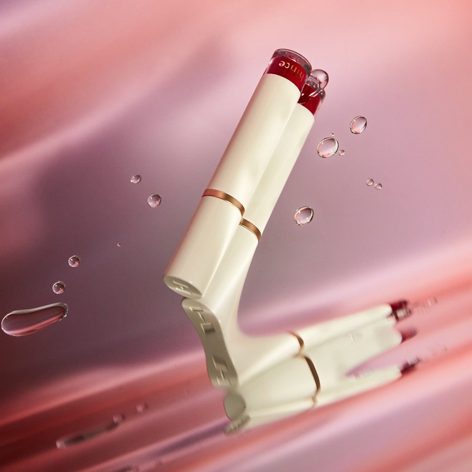 HINCE Mood Enhancer Water Liquid Glow de la marque HINCE, flacon sur fond rose, gouttes et éclats lumineux