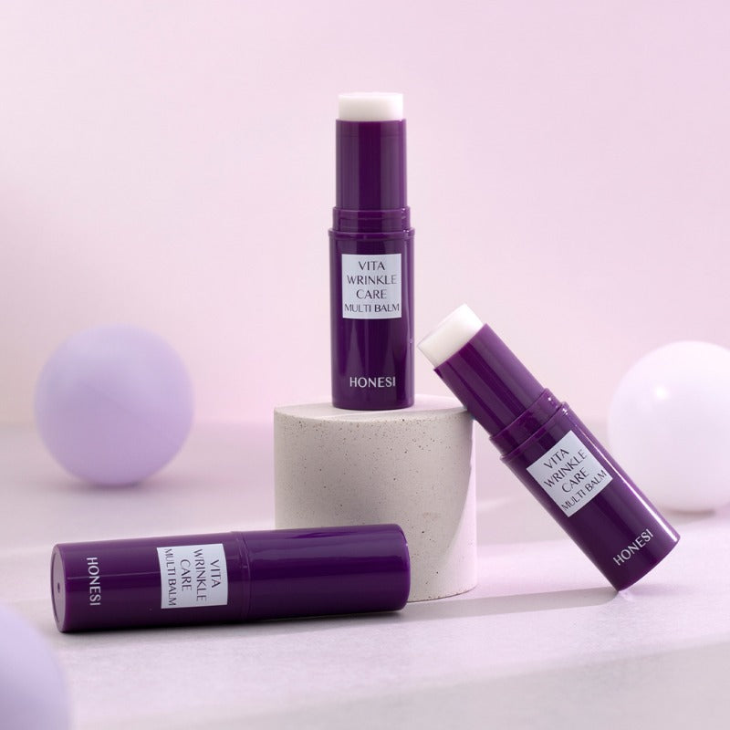 HONESI Vita Wrinkle Care Multi Balm, baume anti-âge en tube violet, sur fond pastel avec boules décoratives