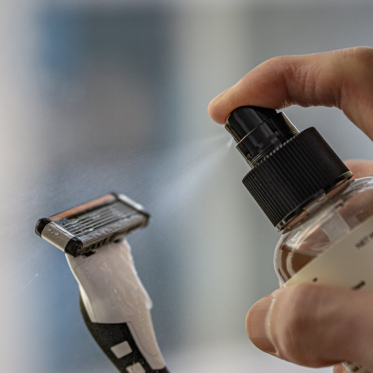 LAZY SOCIETY Razor Blade Sanitizer 120ml : main tenant le spray, rasoirs en arrière-plan, contexte de désinfection.