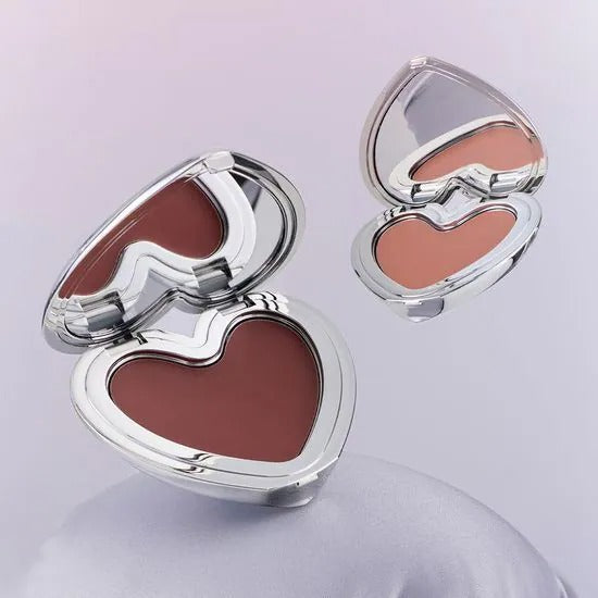 LILYBYRED Love Beam Cheek Mousse, marque LILYBYRED, maquillage joues : deux coques argentées ouvertes, teintes crème sur fond clair.