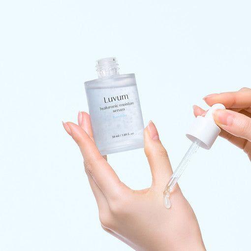 Décris l'image en français : LUVUM Bamboo Hyaluronic Acid Moisture Serum Set 50ml+50ml, mains appliquent le sérum sur fond clair.