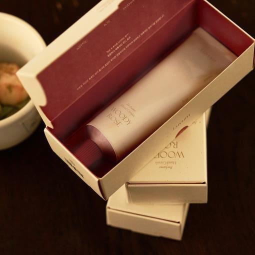Décris l'image en français : LUVUM Woody Rose Perfume Hand Cream 50ml, crème parfumée dans son coffret, sur table.