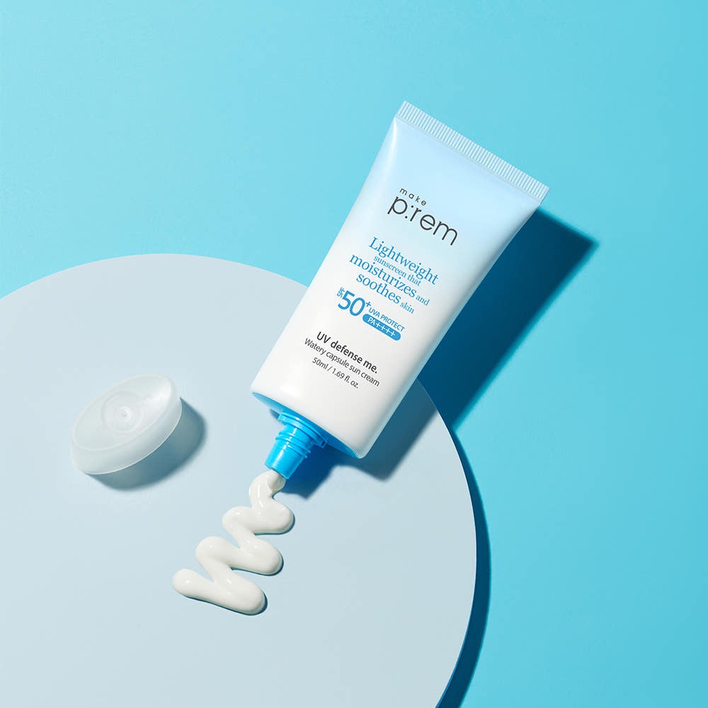 MAKE P:REM UV Defense Me Watery Capsule Sunscreen 50ml SPF50+ PA++++, tube sur fond bleu, main/texture crème blanche