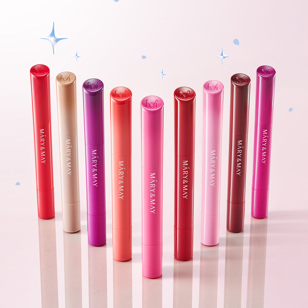 MARY&MAY Blooming Glow Lip 09 Sunset Tangerine 1.7g, sur fond rose avec plusieurs baumes de la marque, étoiles décoratives.