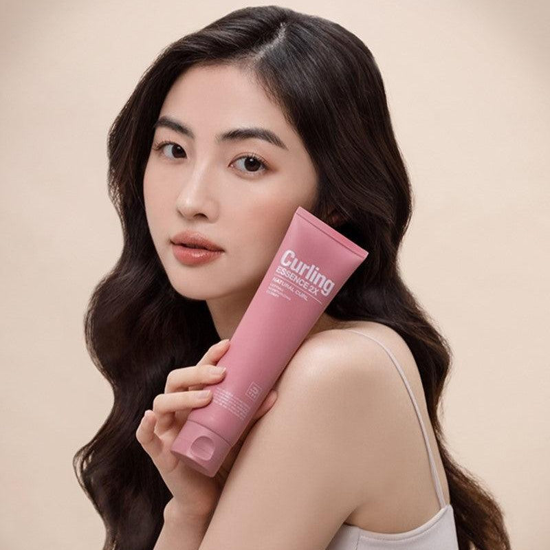 Portrait femme tenant MISE EN SCENE Curling Essence 2X 150ml, tube rose sur fond clair, marque MISE EN SCENE.