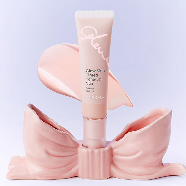 Décrivez l'image en français : MISSHA Glow Skin Tinted Tone-Up Sun 30ml, tube crème en fond clair, mains pastel.