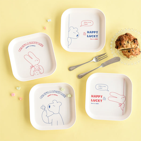 MONOLIKE Happy And Lucky Square Tray, marque MONOLIKE, plateau carré blanc, décorations “Happy & Lucky” sur table jaune.
