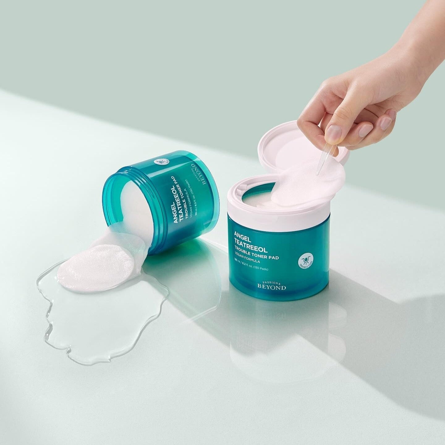 PASSION & BEYOND Angel Tea Tree Trouble Toner Pads 185ml, marque sur pot bleu et mains utilisant des pads sur fond vert