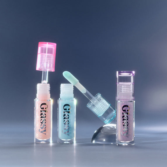 PERIPERA Ink Glazing Lip Gloss Plumper, flacons brillants sur fond bleu, présentation maquillage en studio, marque PERIPERA.